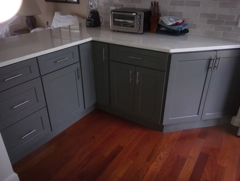Dark gray shaker base cabinets with bar pulls at the peninsula corner, on a reddish wood-look floor.