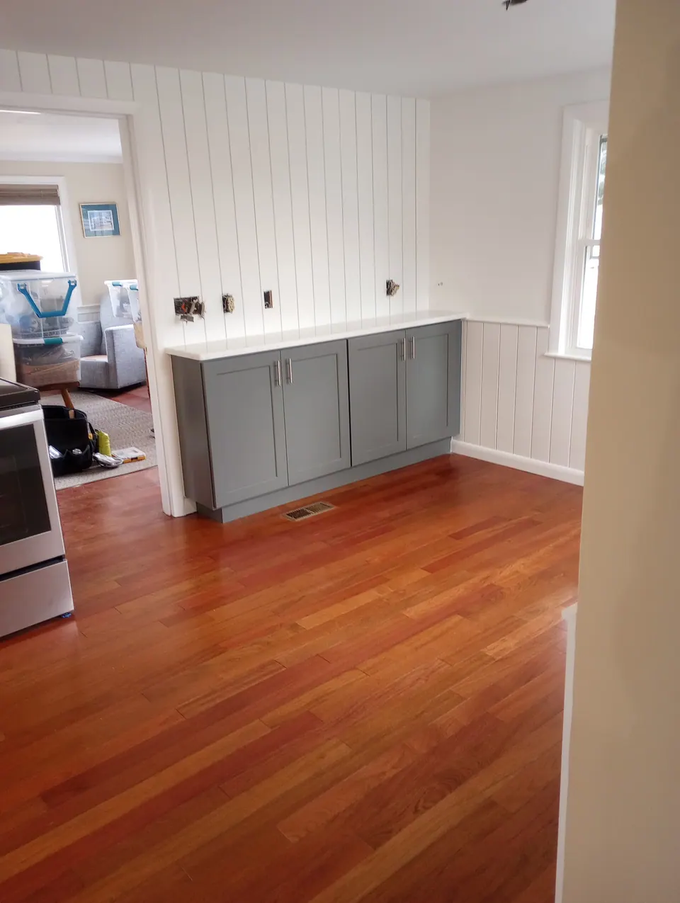 The finished kitchen from the next room: dark gray base cabinets, white wall cabinets and a red oak floor.