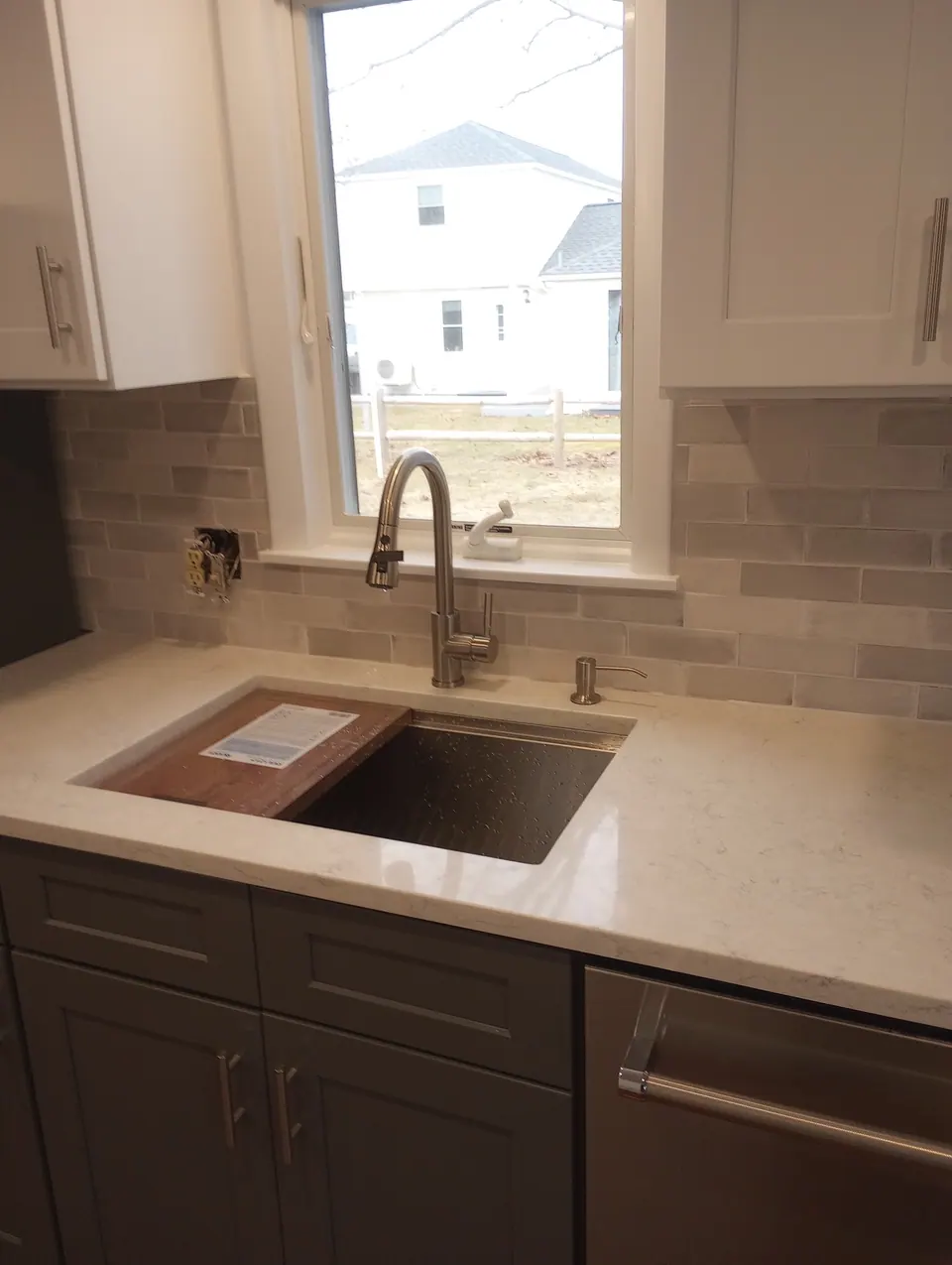 Sink under the window between white wall cabinets, dark gray base cabinets below.