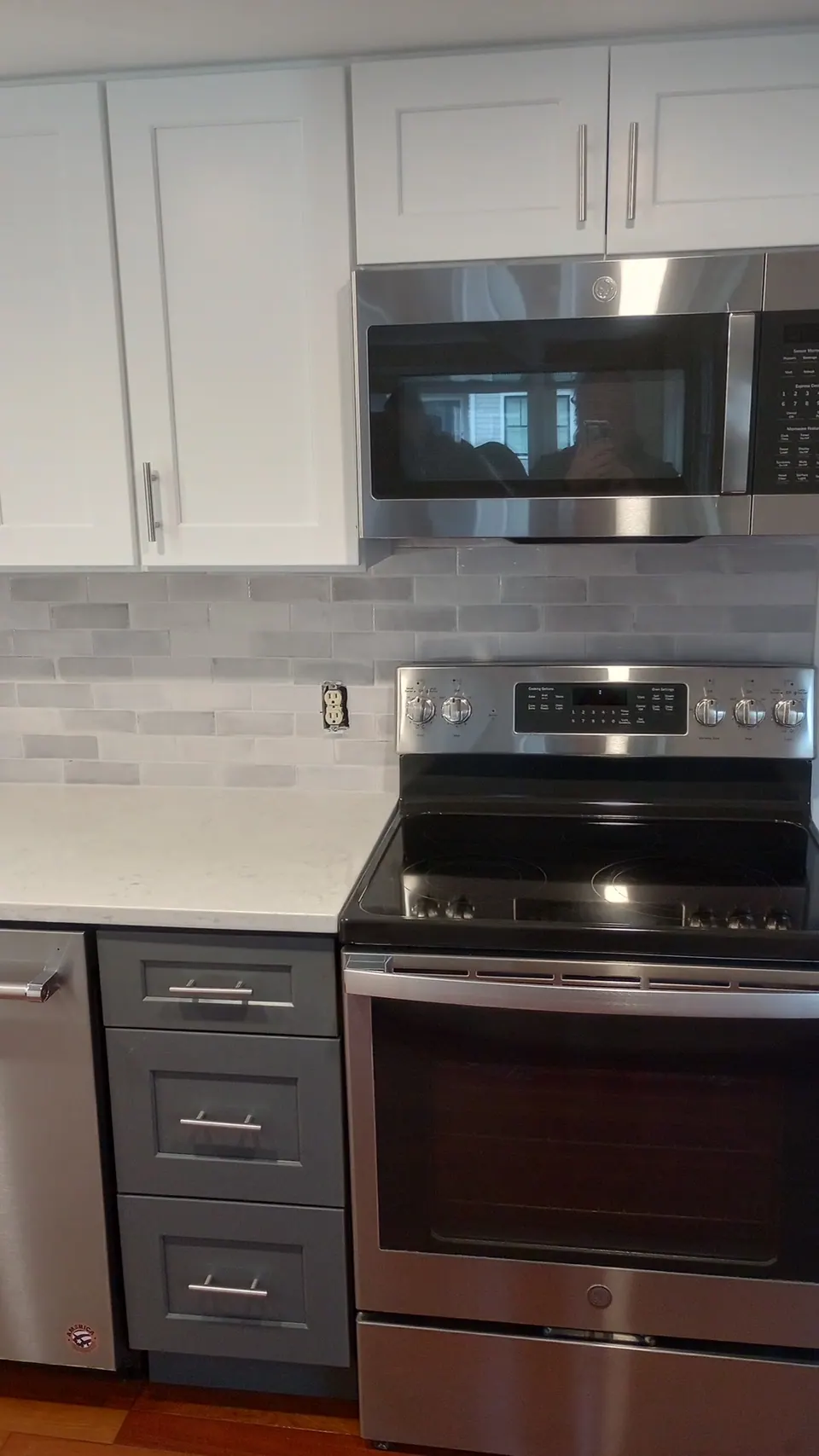 Stainless range between dark gray drawer bases, white wall cabinets and microwave above.