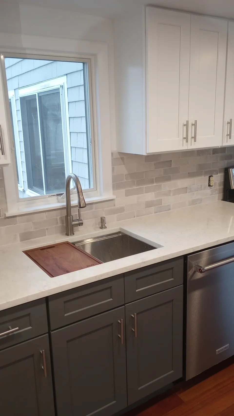 Undermount sink and dishwasher in the dark gray base run with a gray brick-pattern backsplash.