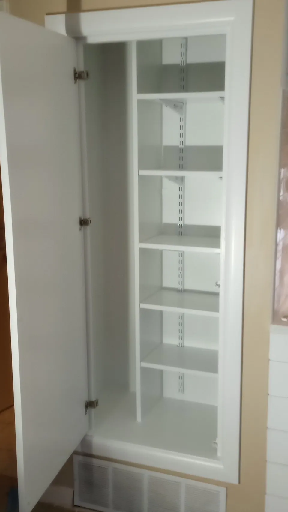 Tall white pantry cabinet open, with adjustable shelves inside.