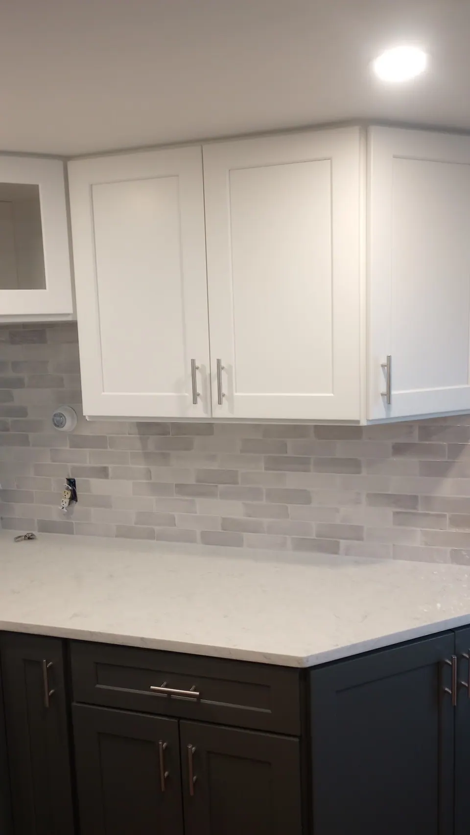 Corner of white wall cabinets over dark gray base cabinets and a white quartz top.