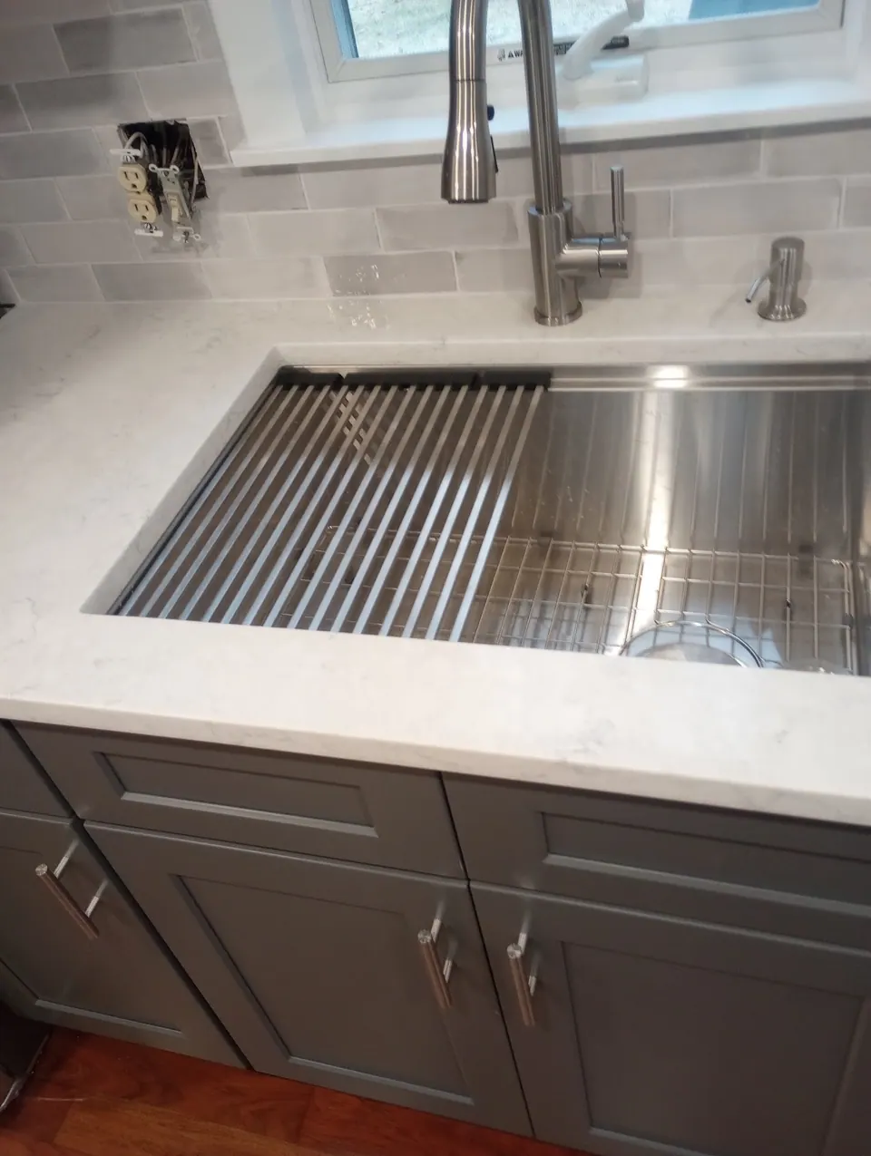 Workstation sink with a roll-up drying rack in the white quartz counter.