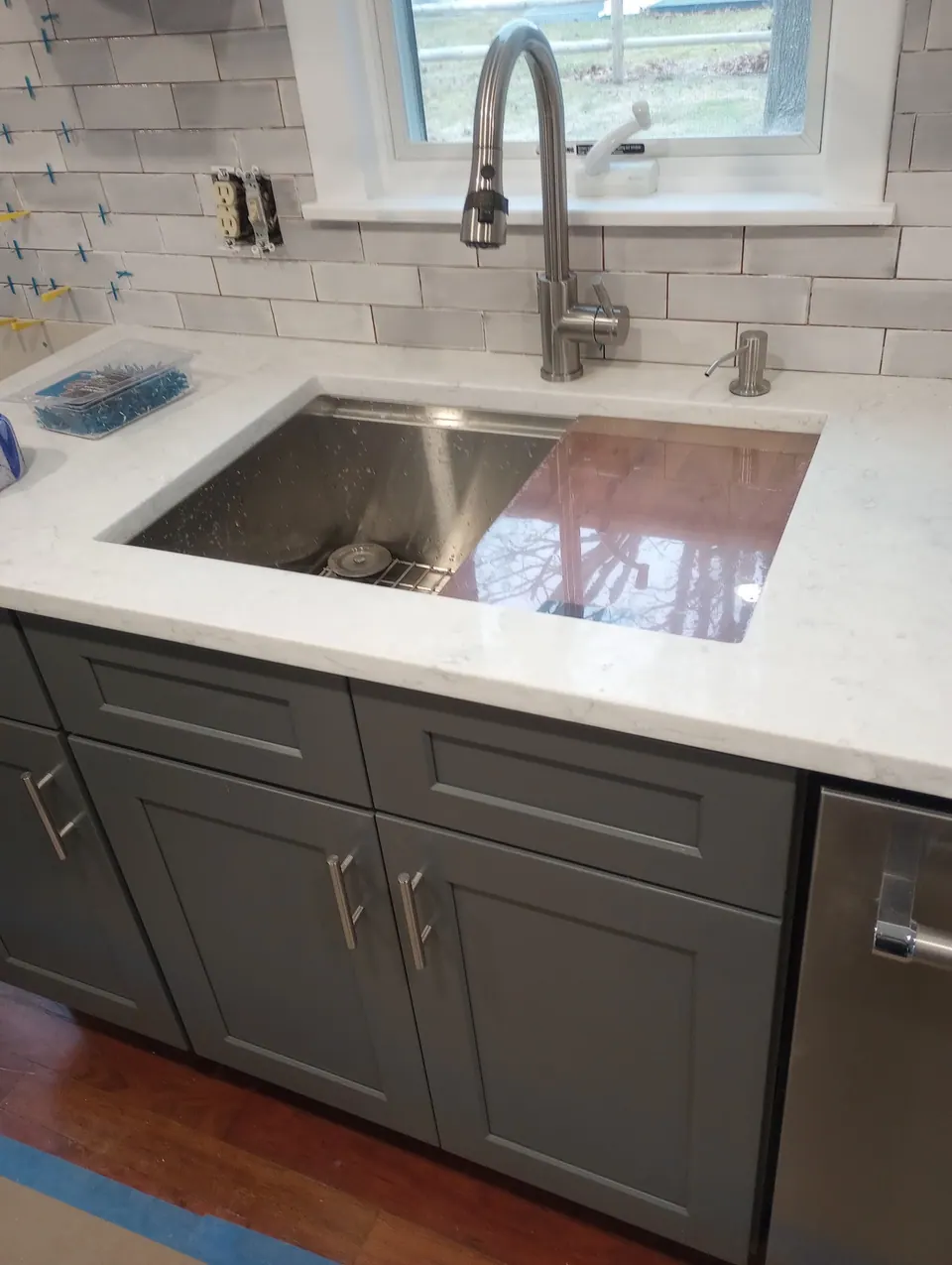 Stainless sink and pull-down faucet in the white quartz counter over dark gray cabinets.