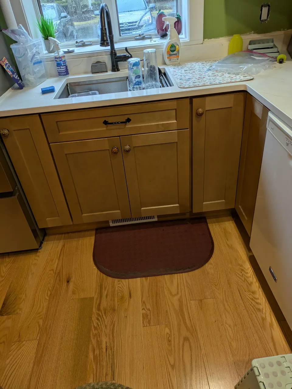 Light wood sink base cabinet under an undermount sink with dark faucet, wood floor below.
