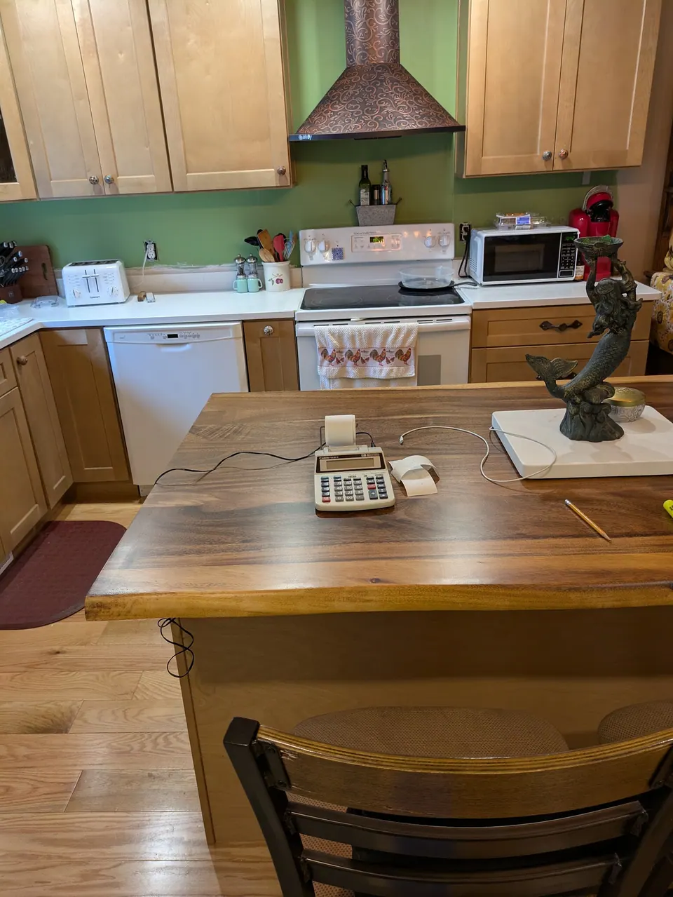 View across the dark wood island top to the range wall with light wood cabinets and copper-tone hood.