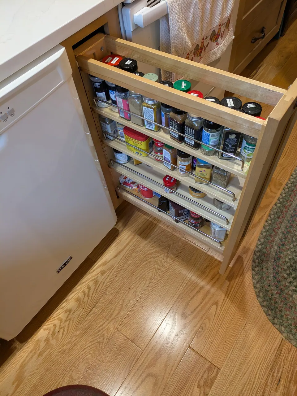 Narrow pull-out spice rack between the dishwasher and range, filled with spice jars.