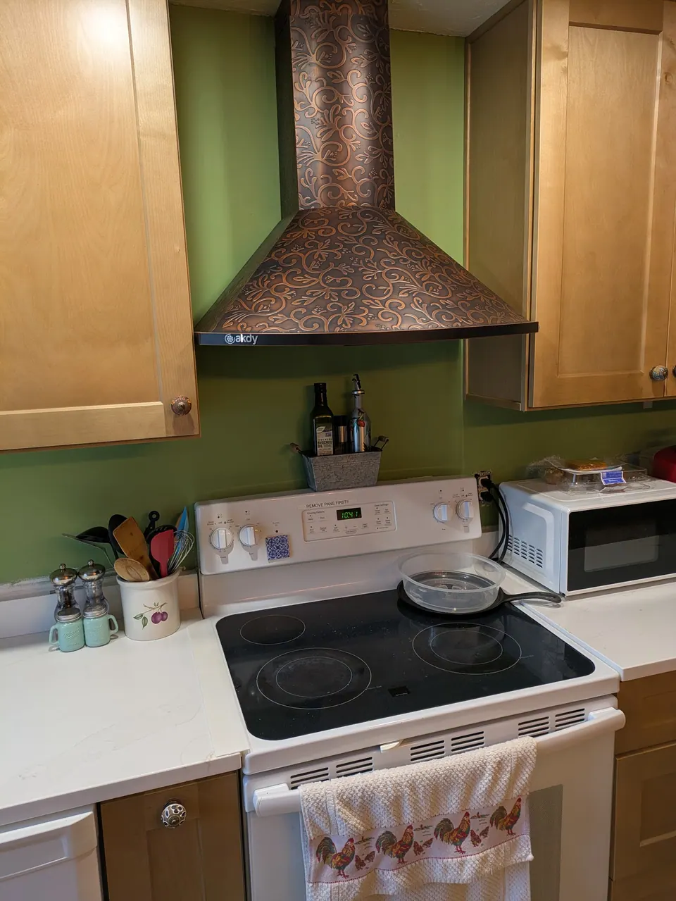 Embossed copper-tone range hood between light wood wall cabinets above a white range and countertop.