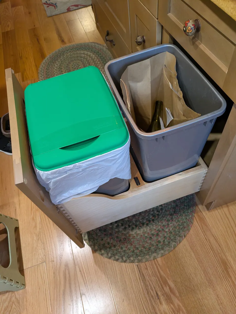 Pull-out trash drawer in the island with two bins, one with a green lid.