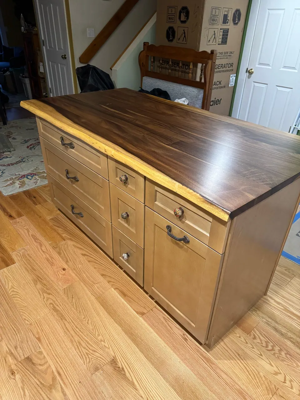 In progress: island with light wood drawers and a dark live-edge wood top, appliance boxes behind.