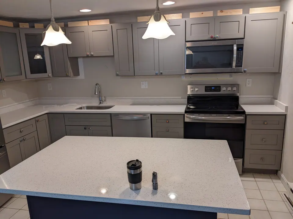 Gray shaker kitchen with a navy island, pendant lights and stainless appliances.