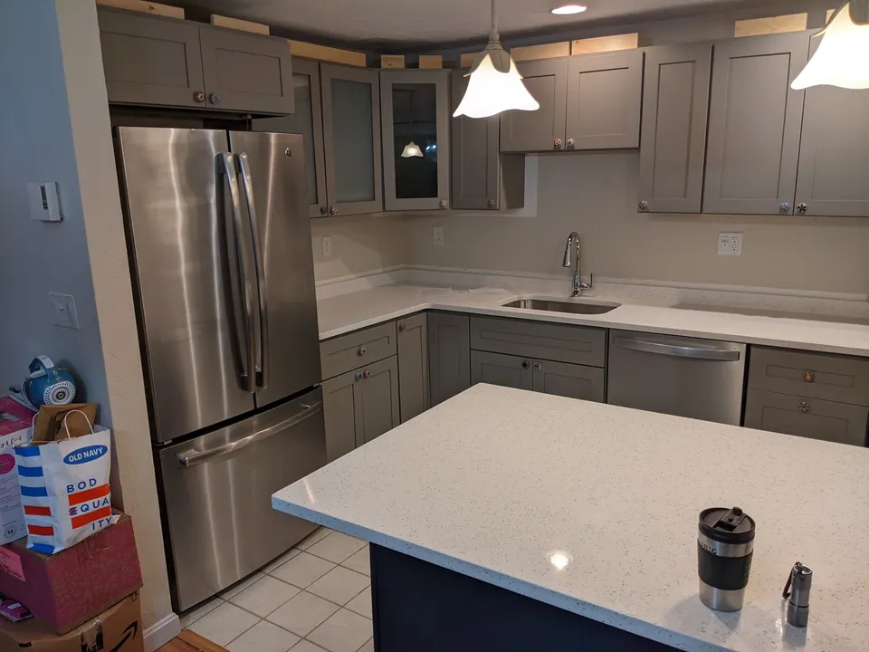 The navy island with a white quartz top in front of the gray cabinets.