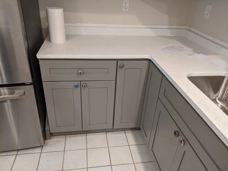 Corner of gray shaker base cabinets with a white quartz top.
