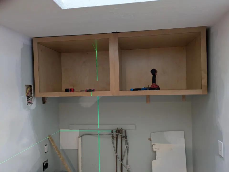 Wall cabinet boxes hung on a bare wall, leveled with a green laser line.