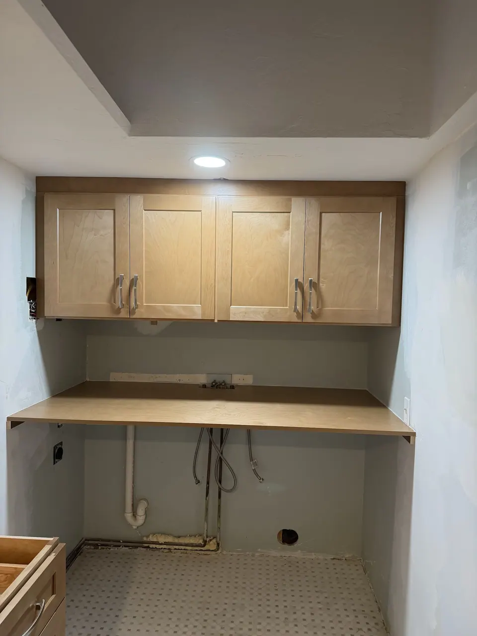 Wall cabinets over a wood counter in the recess, before the plumbing is finished.