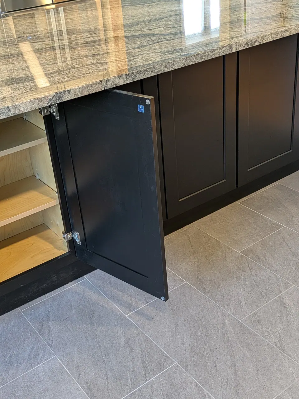 Black shaker base cabinet door open under the countertop overhang, showing shelves inside.