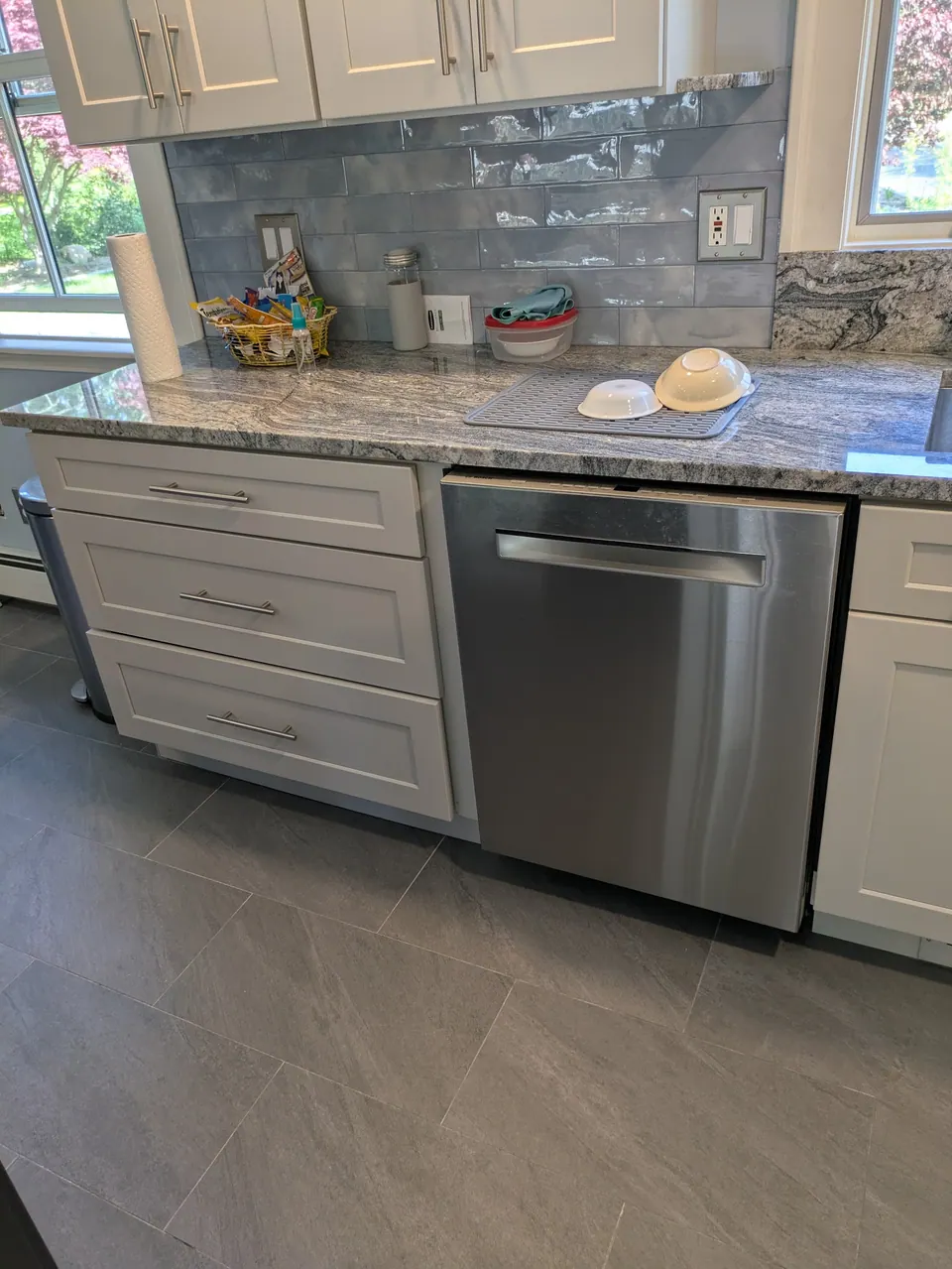 Light gray three-drawer base and stainless dishwasher under a gray veined countertop.