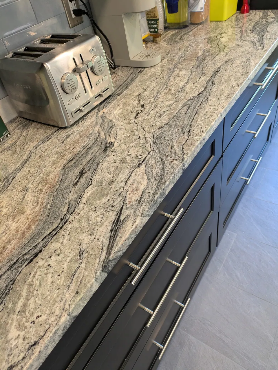 Gray veined countertop edge above black drawer fronts with long brushed bar pulls.