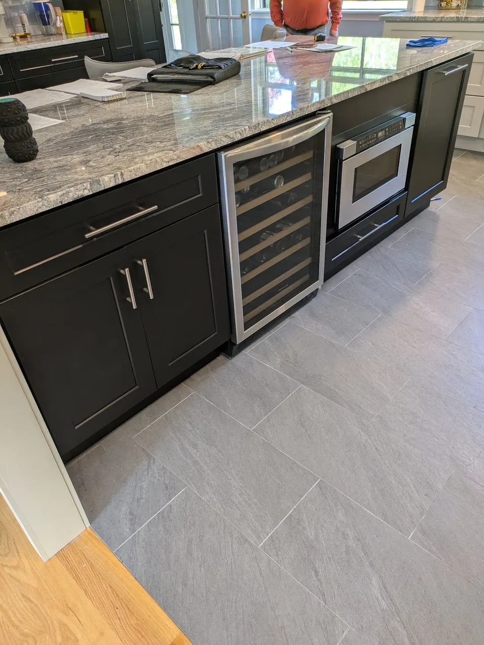 Black peninsula with wine cooler and microwave drawer under a gray veined countertop.