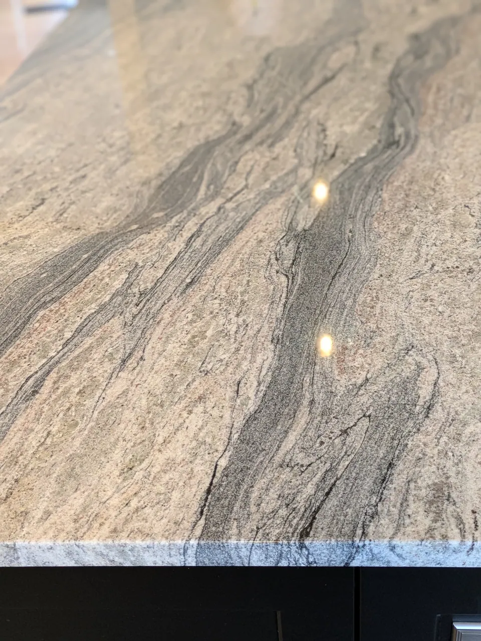 Polished gray countertop with dark wavy veining above a black cabinet.