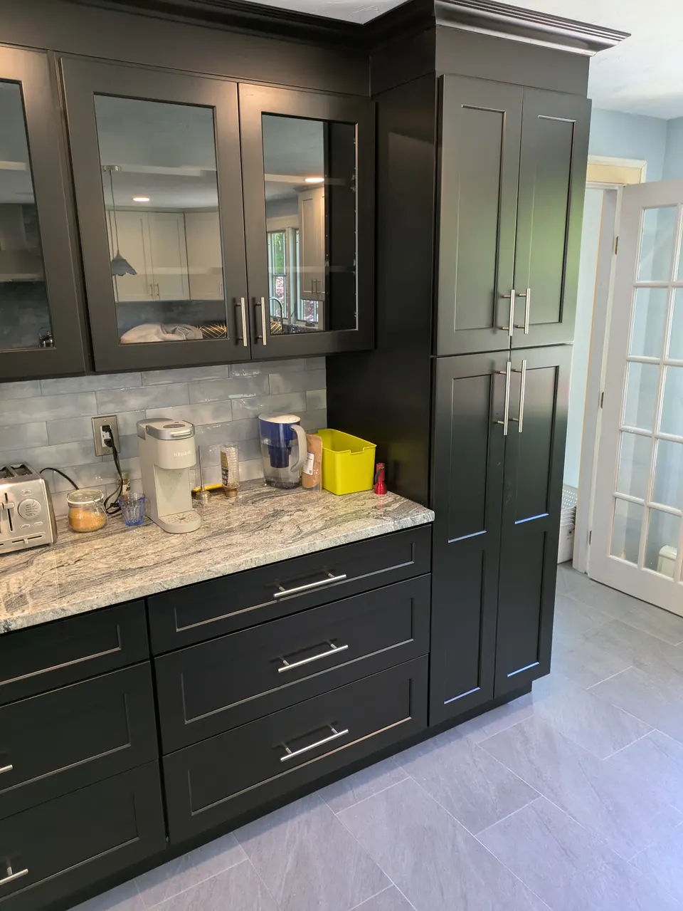 Black glass-front wall cabinets over drawer bases beside a tall black pantry cabinet.