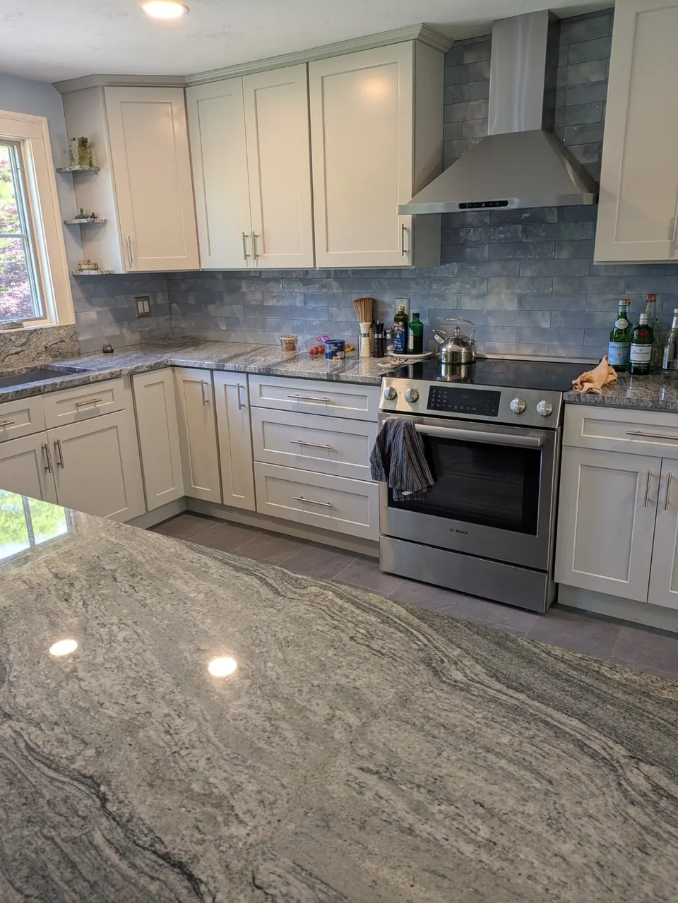 Light gray shaker cabinets around a stainless range and chimney hood, blue tile backsplash.