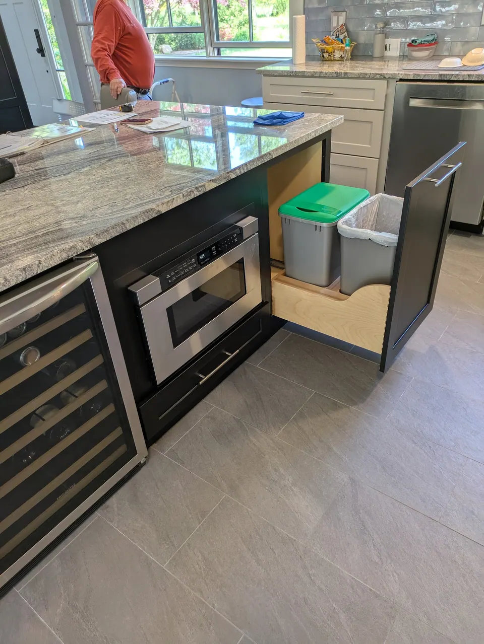Black pull-out with two trash bins beside the microwave drawer and wine cooler.