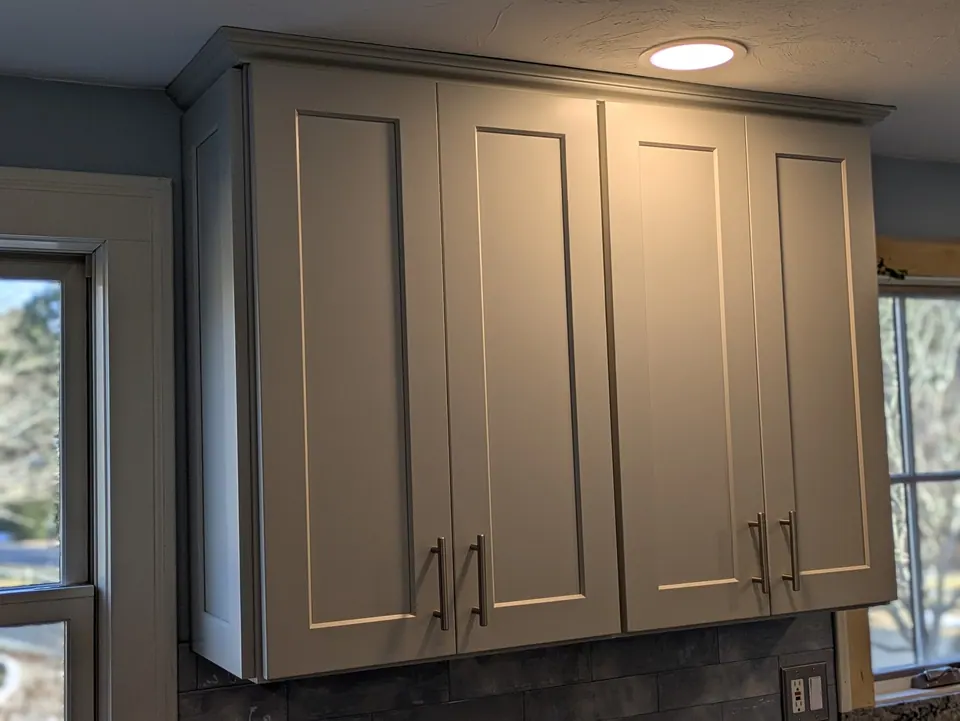 Light gray wall cabinets with crown molding between two windows.