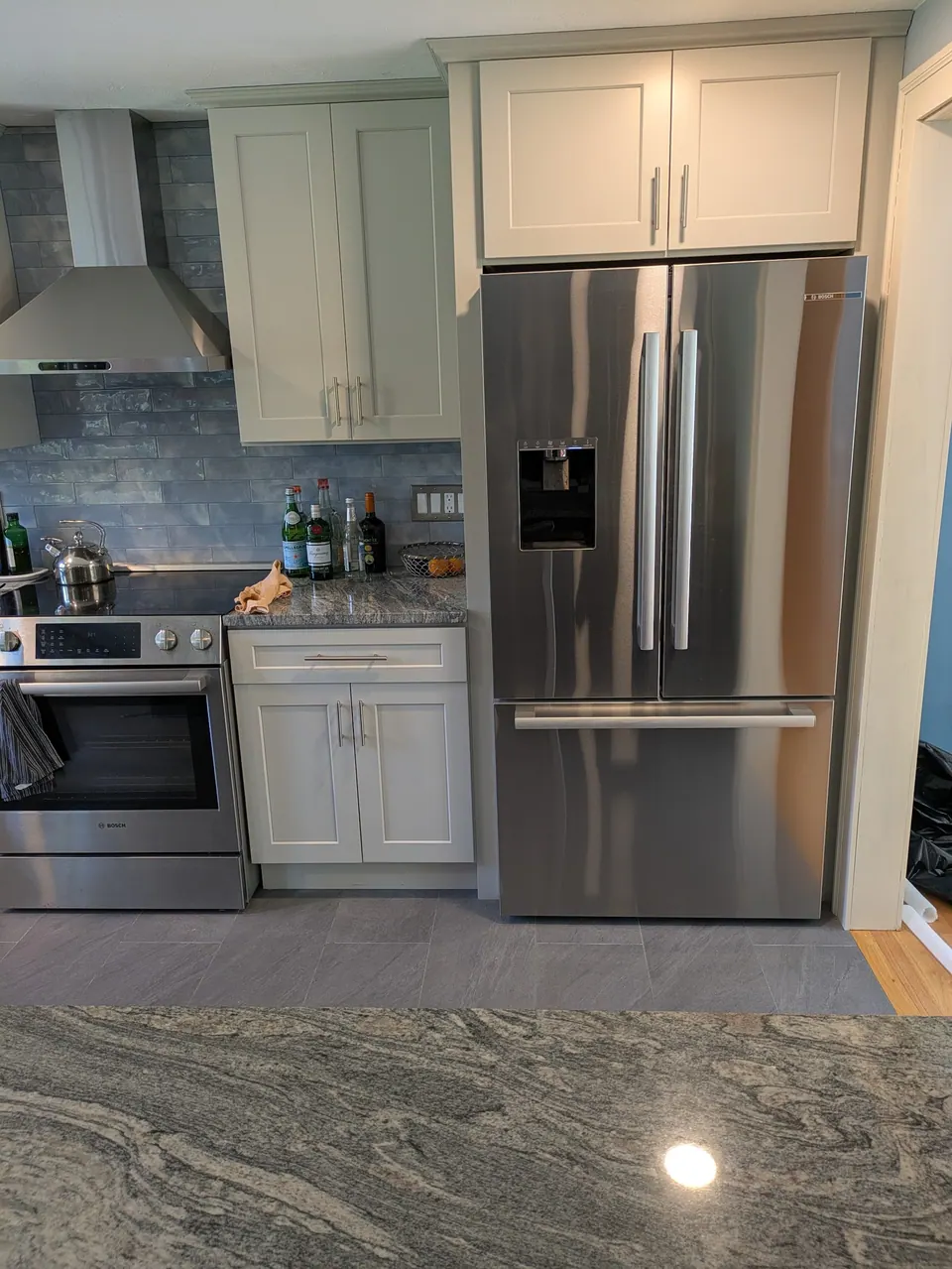 Stainless refrigerator with a light gray cabinet above, wall cabinet and range beside it.