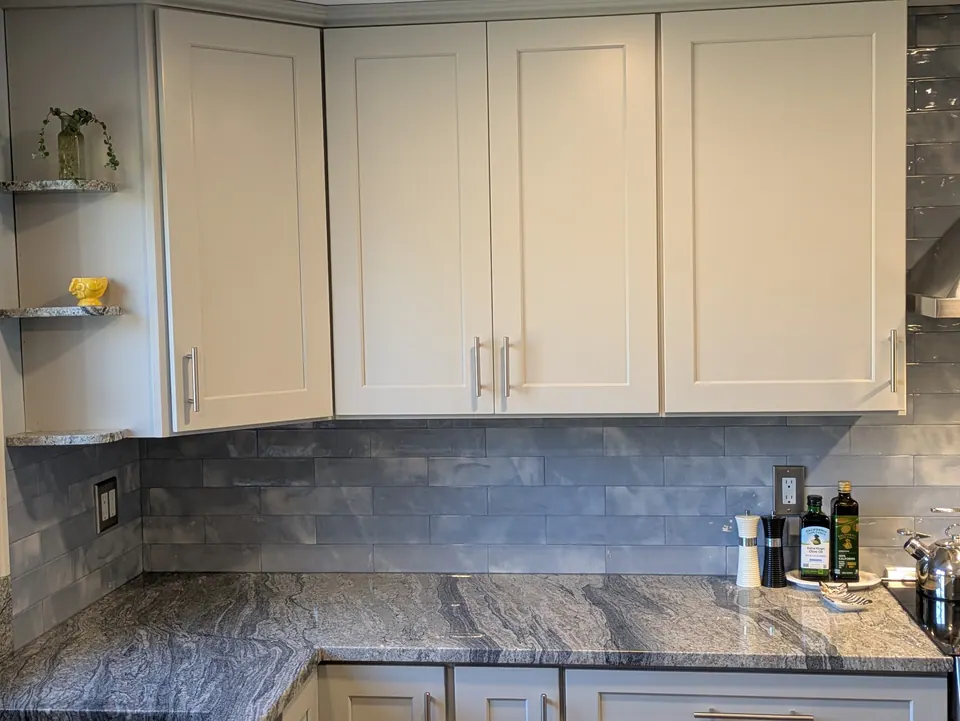 Light gray corner wall cabinets with crown molding above a gray veined countertop.