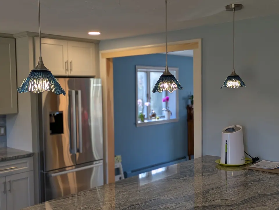 Three blue pendant lights over the peninsula, light gray cabinets blurred behind.