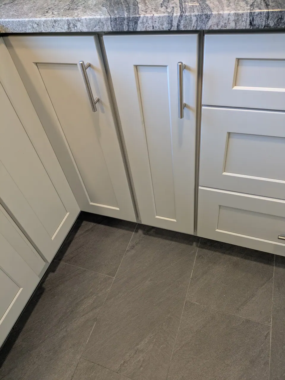 Light gray base cabinets meeting at an inside corner, narrow doors and drawers.