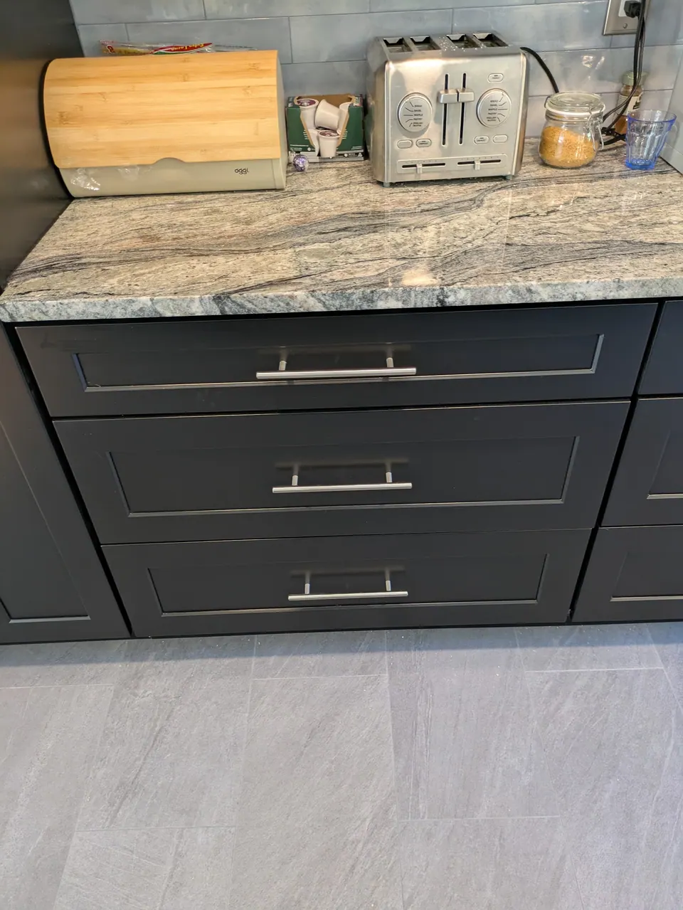 Black three-drawer base with bar pulls under a gray veined countertop.