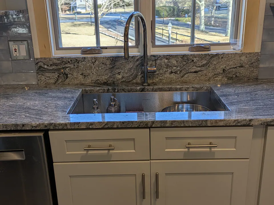 Undermount stainless sink and chrome faucet below a window, light gray sink base.