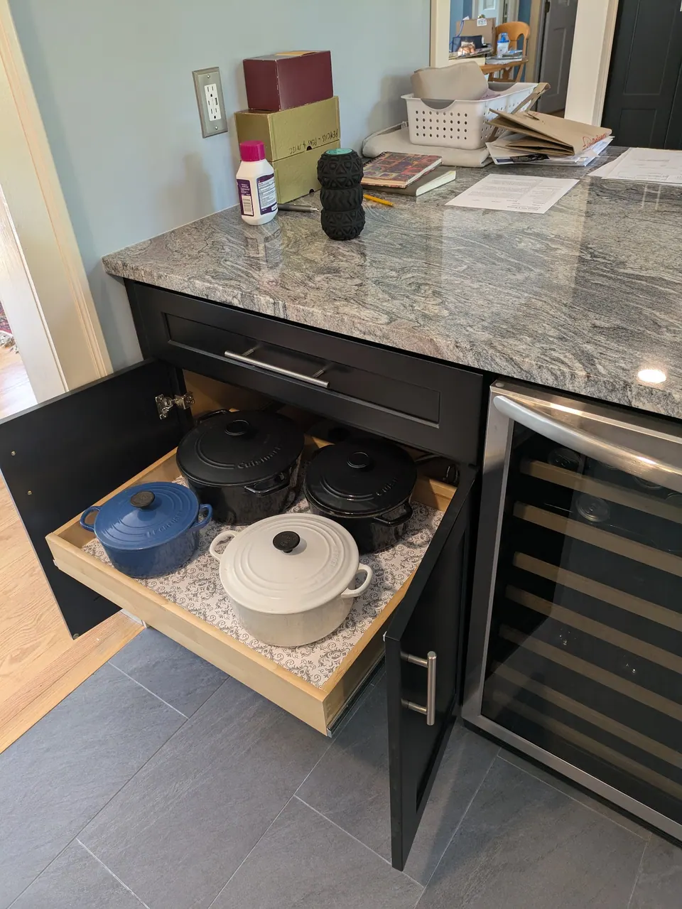 Black base cabinet open with a wood roll-out tray holding four lidded pots.