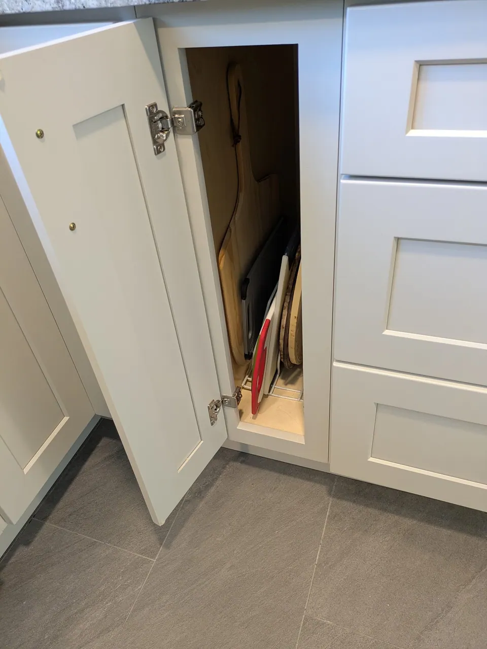Narrow light gray base cabinet open, with cutting boards stored upright inside.