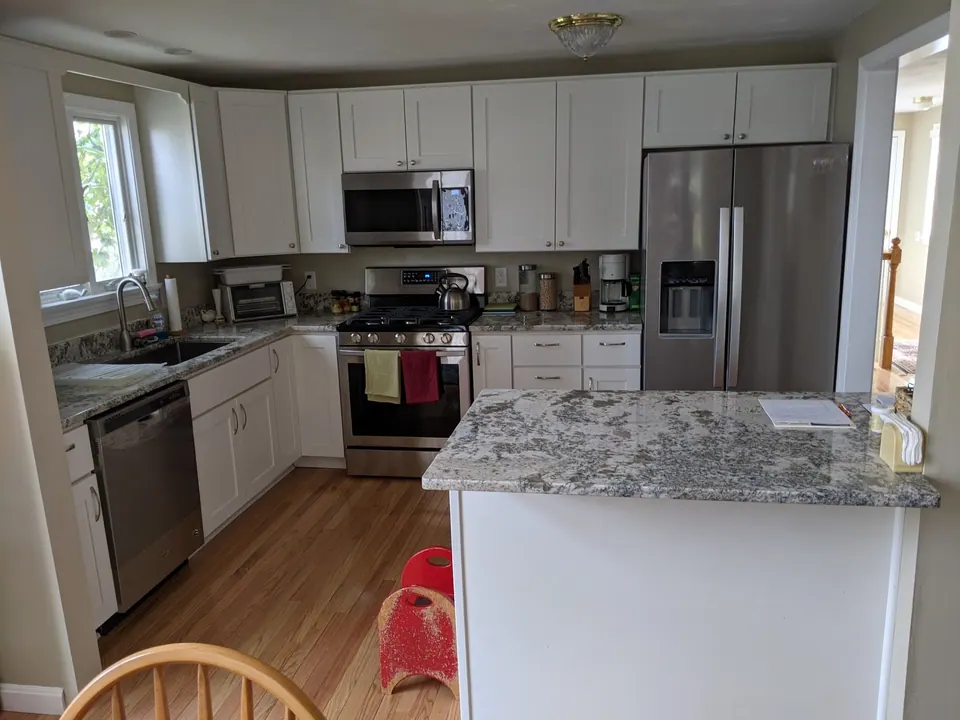 White shaker kitchen open to the dining room, granite peninsula in front.