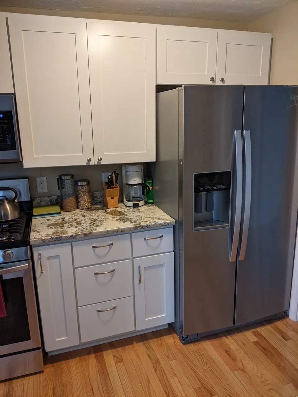 Stainless refrigerator beside white shaker wall and base cabinets.