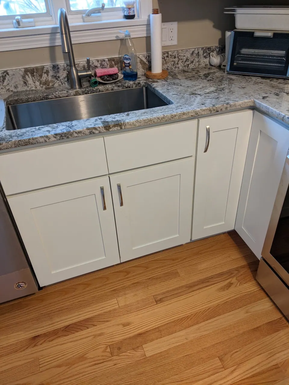 Sink run of white shaker cabinets under a granite counter.