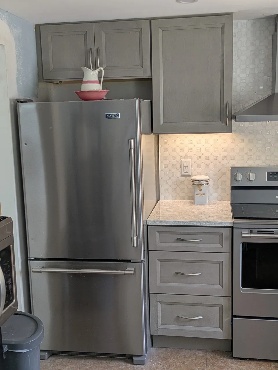 Stainless refrigerator beside a gray three-drawer base and range, gray wall cabinets above.