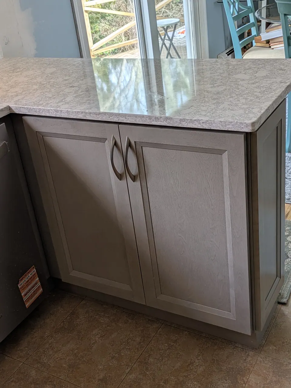 Gray two-door base cabinet at the end of the counter, light marbled countertop above.