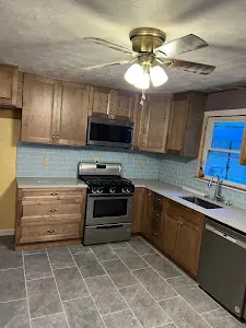 L-shaped kitchen with brown wood cabinets, gas range, microwave above and sink under a window.