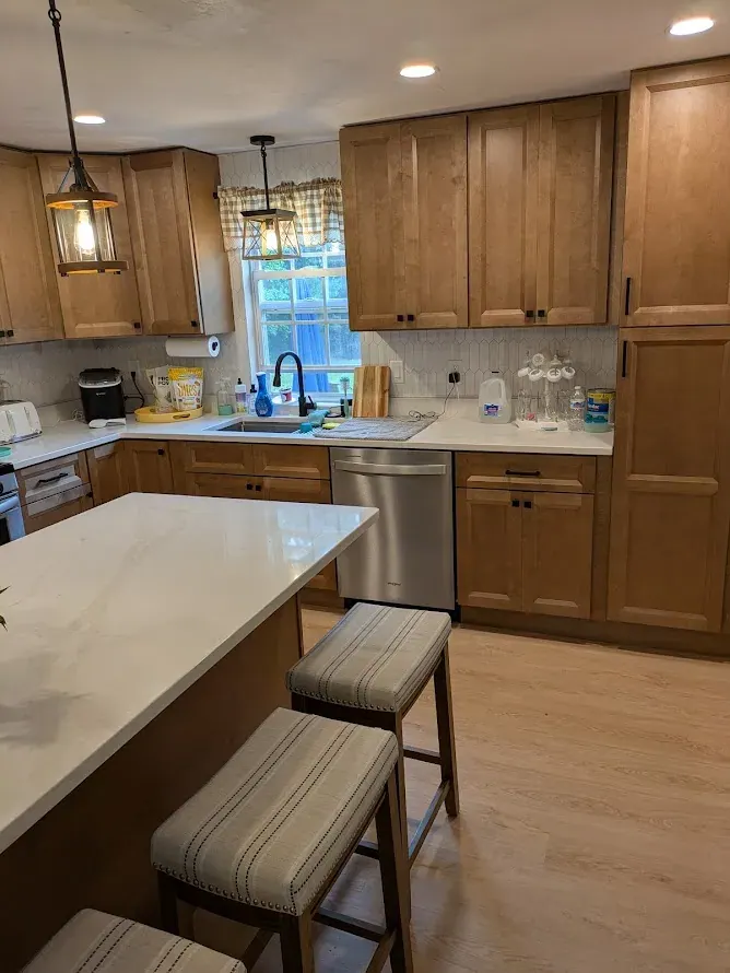 Brown wood cabinets along the sink wall with a tall pantry, white island countertop in front.