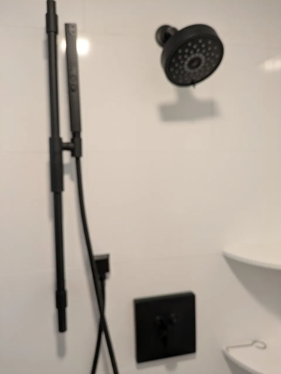Matte black shower head, hand shower on a slide bar and valve on white wall tile.