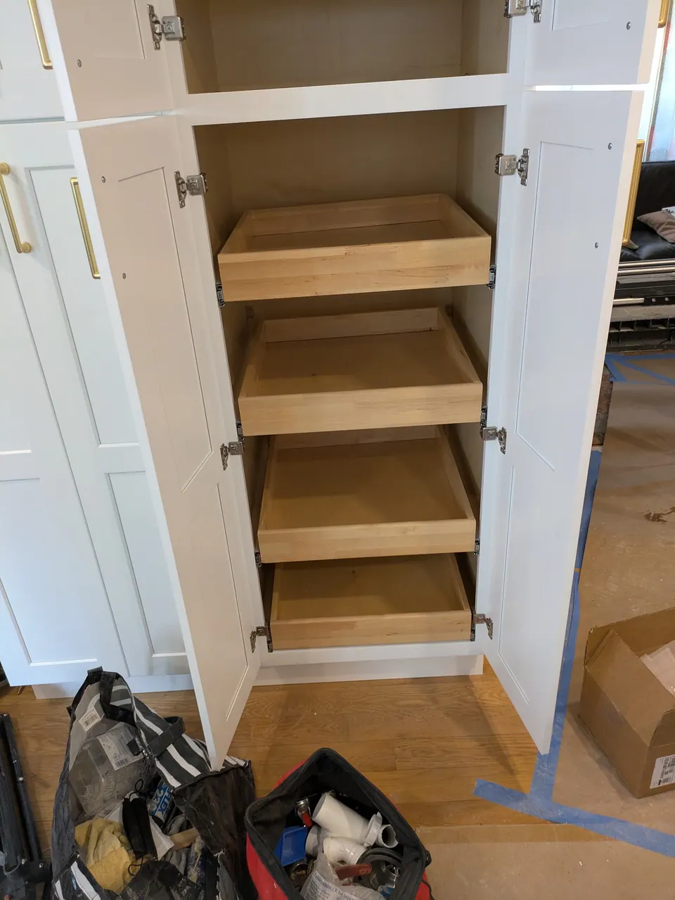 Tall white pantry cabinet with doors open, showing four wood roll-out trays.