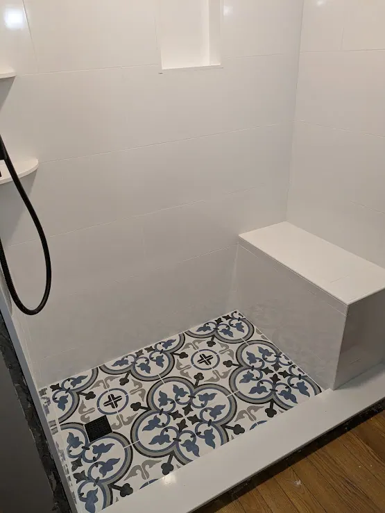 Finished tiled shower with white wall tile, built-in bench, niche and blue patterned floor tile.