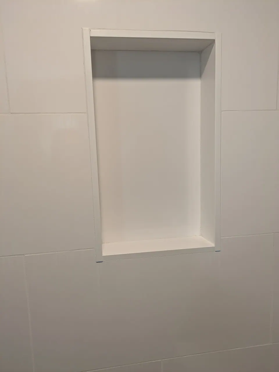 Recessed niche in a white tiled shower wall.