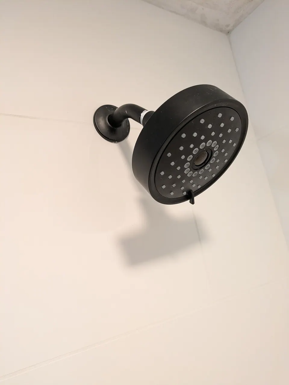 Matte black round shower head on a white tiled wall.