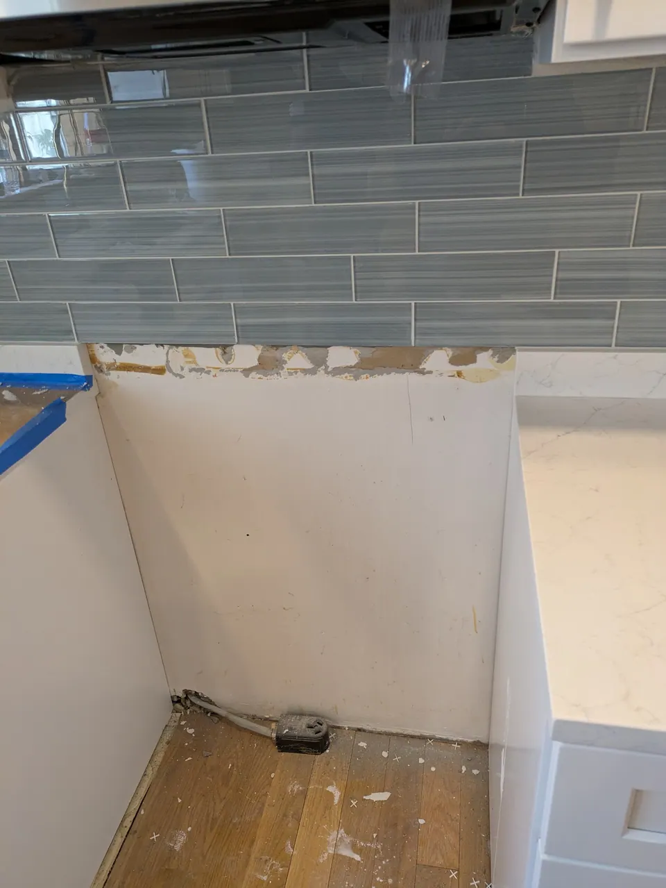Empty appliance opening between white cabinets under a gray tile backsplash, wall unfinished below the tile.